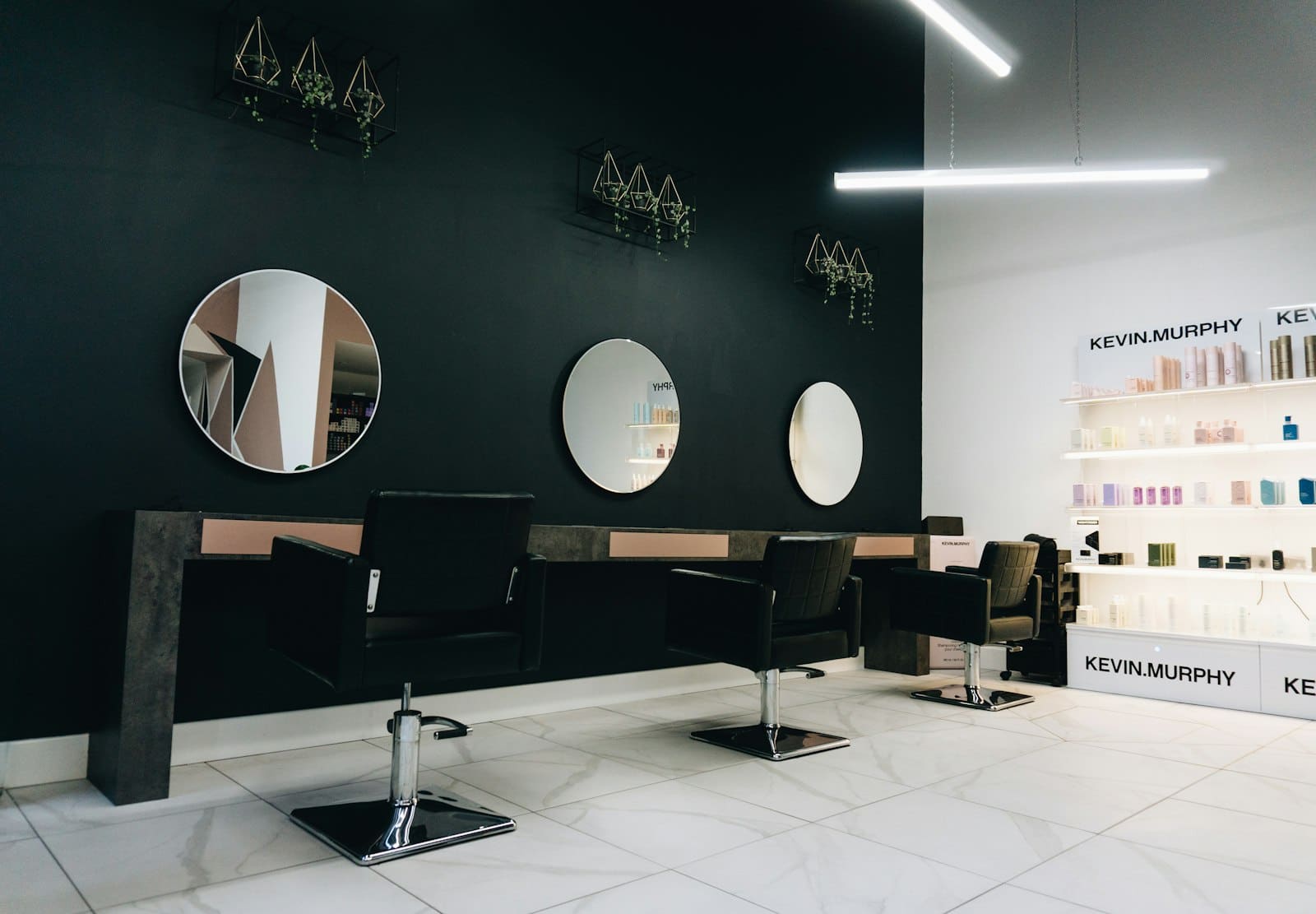 Interior del salón: pared negra con espejos redondos y sillones de peluquería
